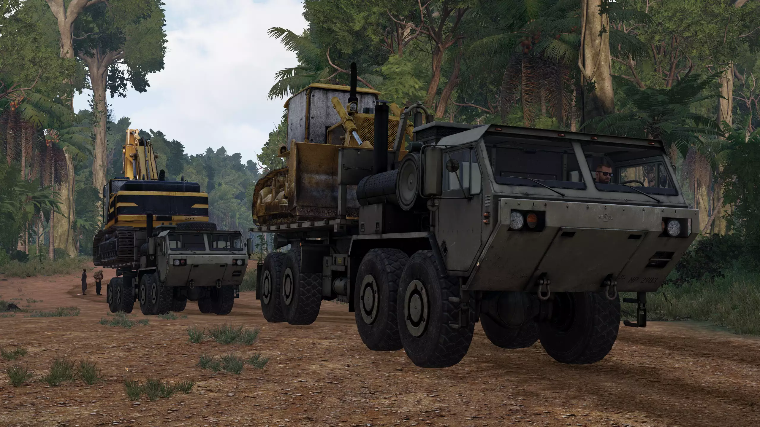 two HEMTTs carry construction equipment through a jungle